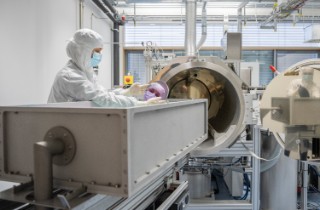 Eine Forscherin mit Labor-Schutzausrüstung  hält einen hochreflektierenden Spiegel für Laseranwendungen in der Hand. 